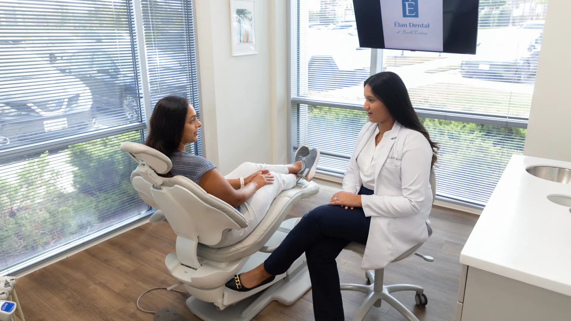 Dentist consulting with patient in a modern dental office with large windows and natural light.