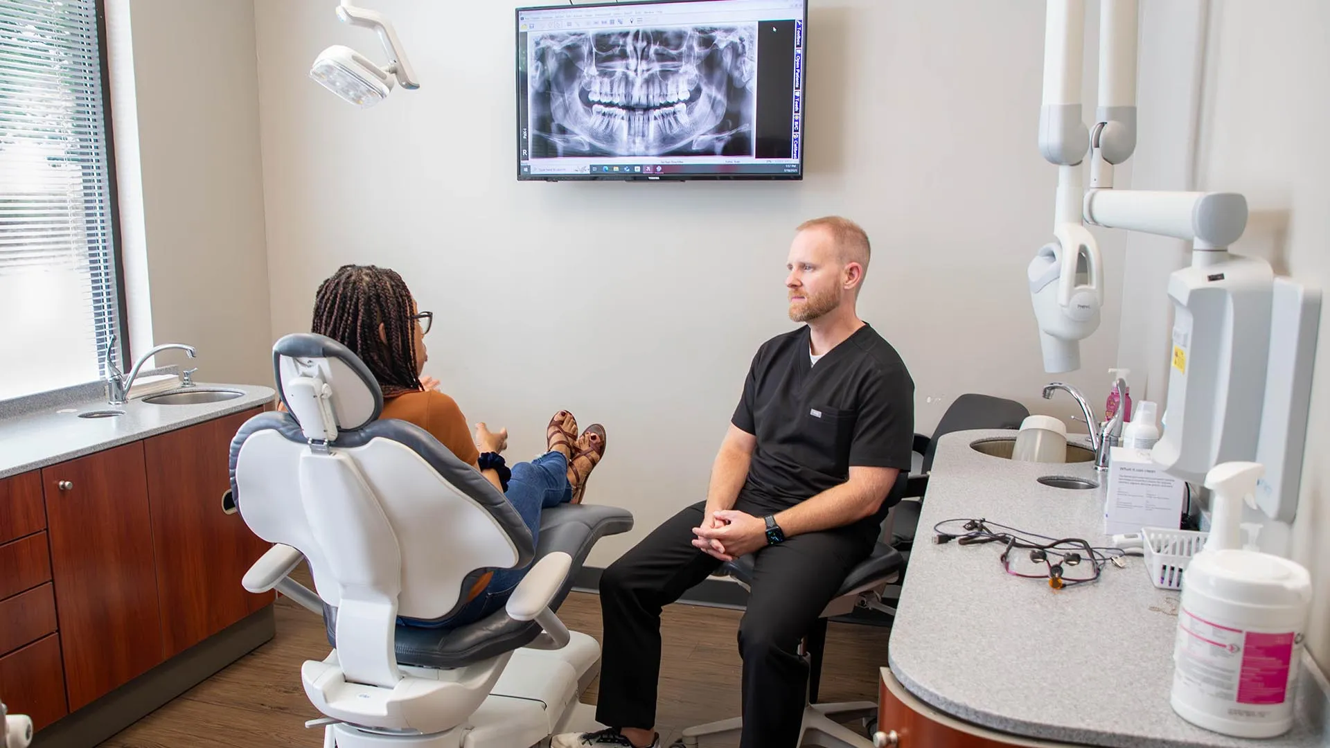 Dentist consulting patient in dental office with mouth x-ray displayed on screen in the background