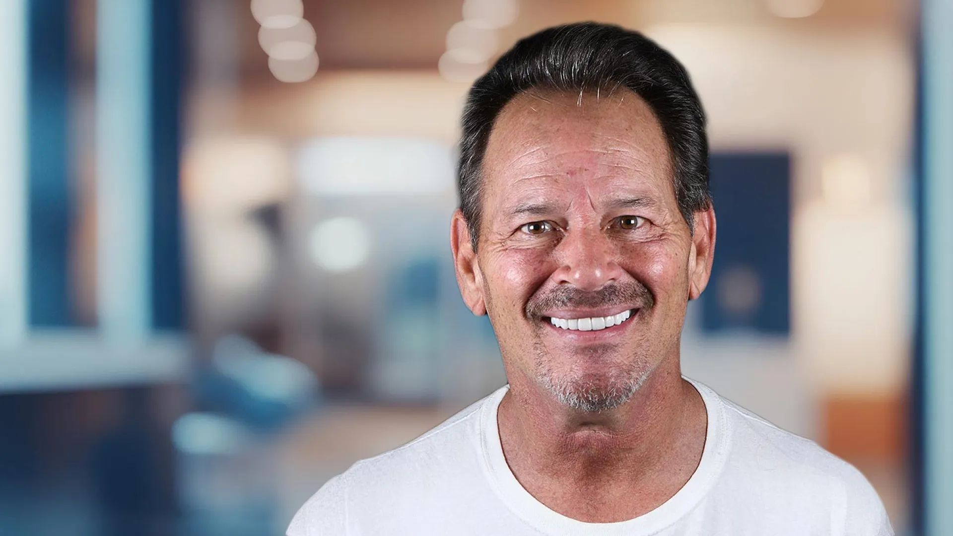 Smiling man in a casual shirt against a blurred indoor background.