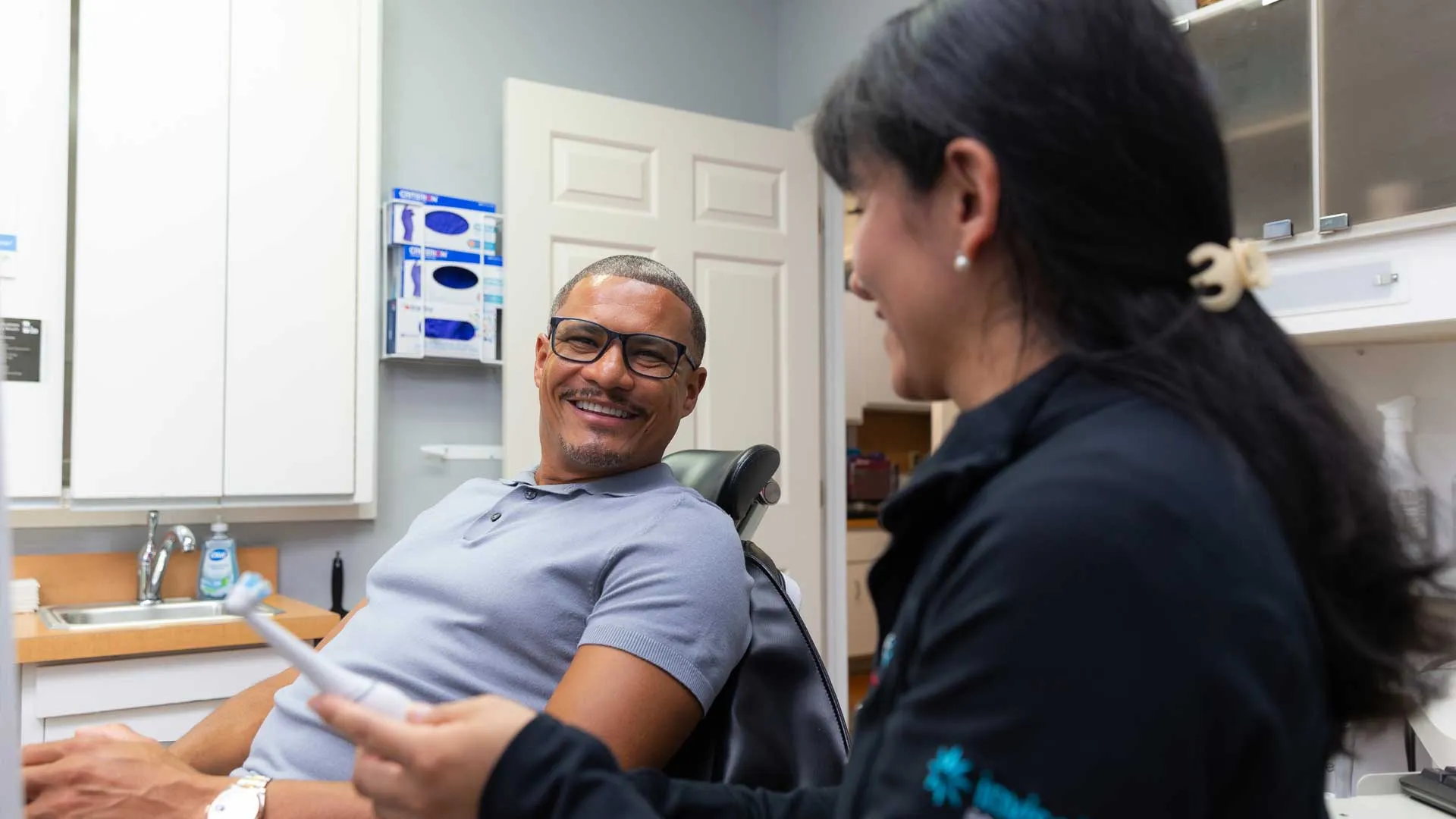 Smiling man in a dental chair talking with a female dental professional in a clinic consultation room.