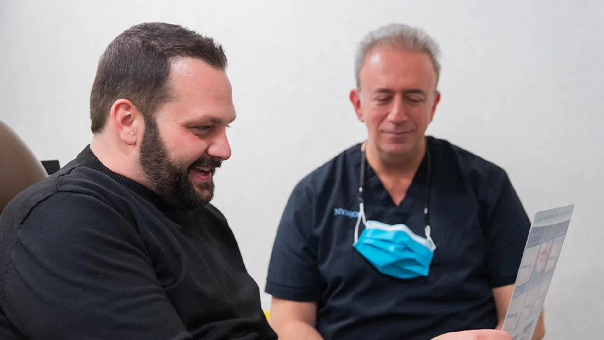 Man discussing treatment options with a male healthcare professional wearing scrubs and a face mask around his neck.