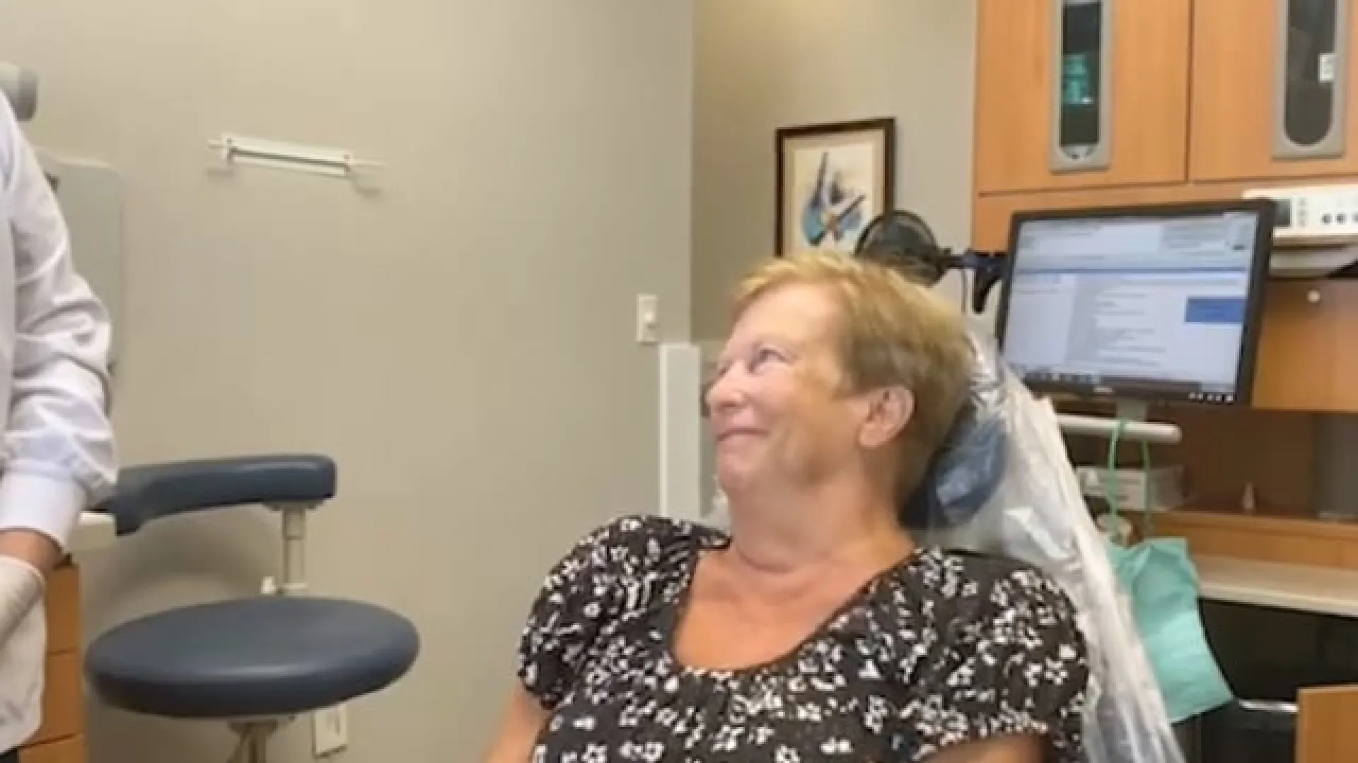 Smiling woman sitting in dental chair during a dental checkup with equipment and computer visible in the background