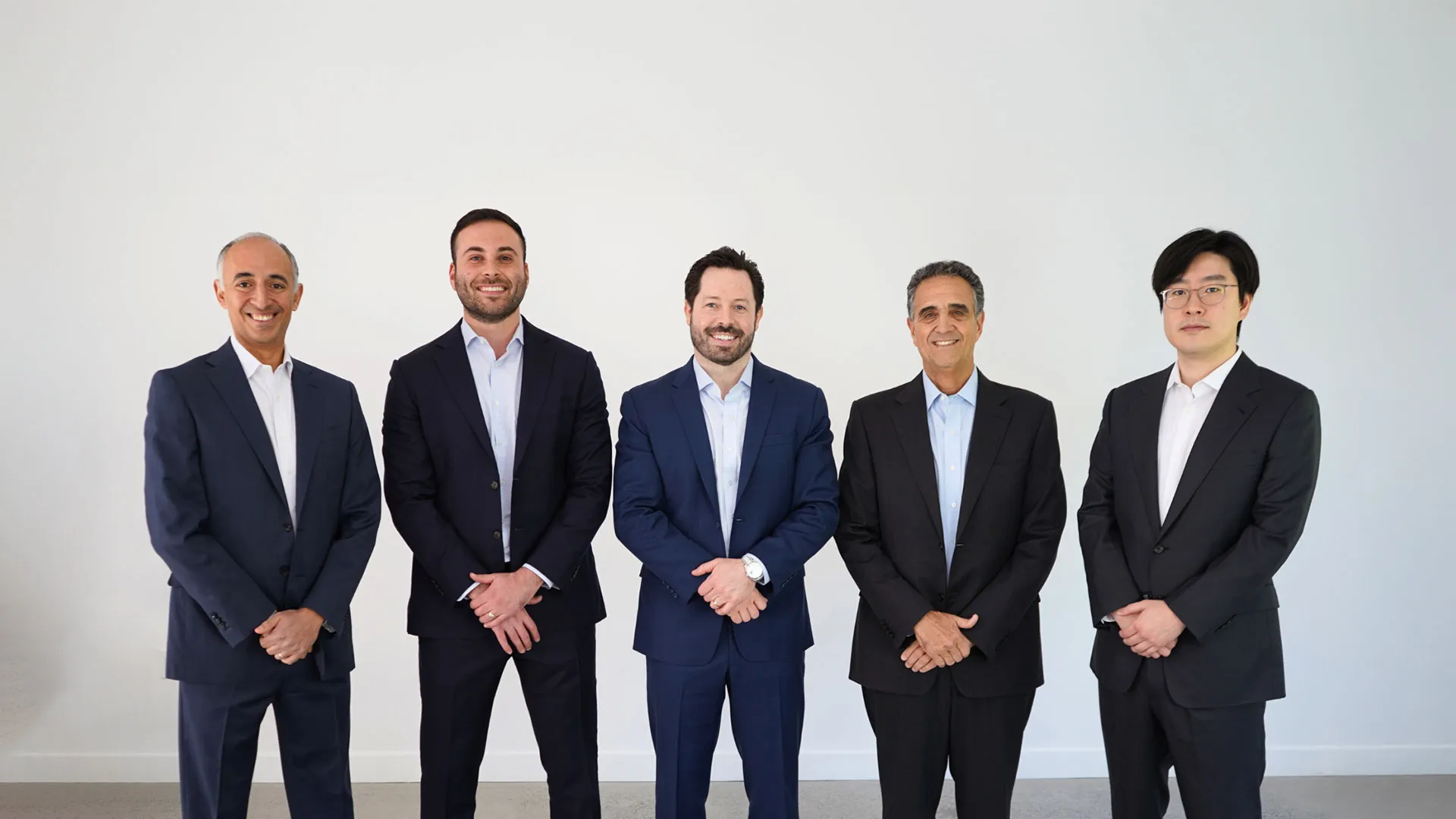 Five business professionals in suits standing together in a modern office setting.