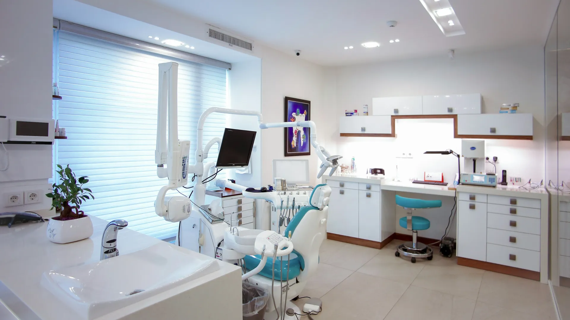 Bright modern dental clinic with white cabinets, dental chair, equipment, and clean workspace under natural light.