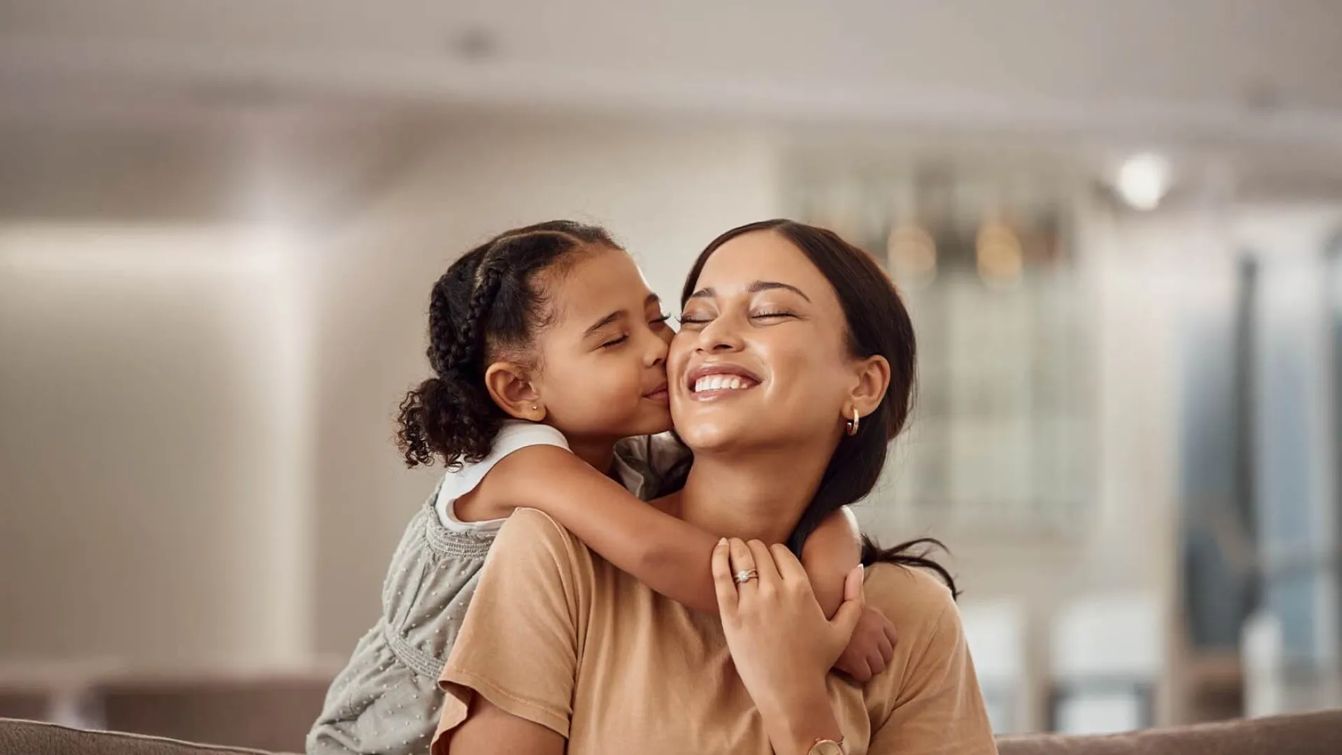 Young girl hugging and kissing her smiling mother in a cozy home setting, showing love and affection.
