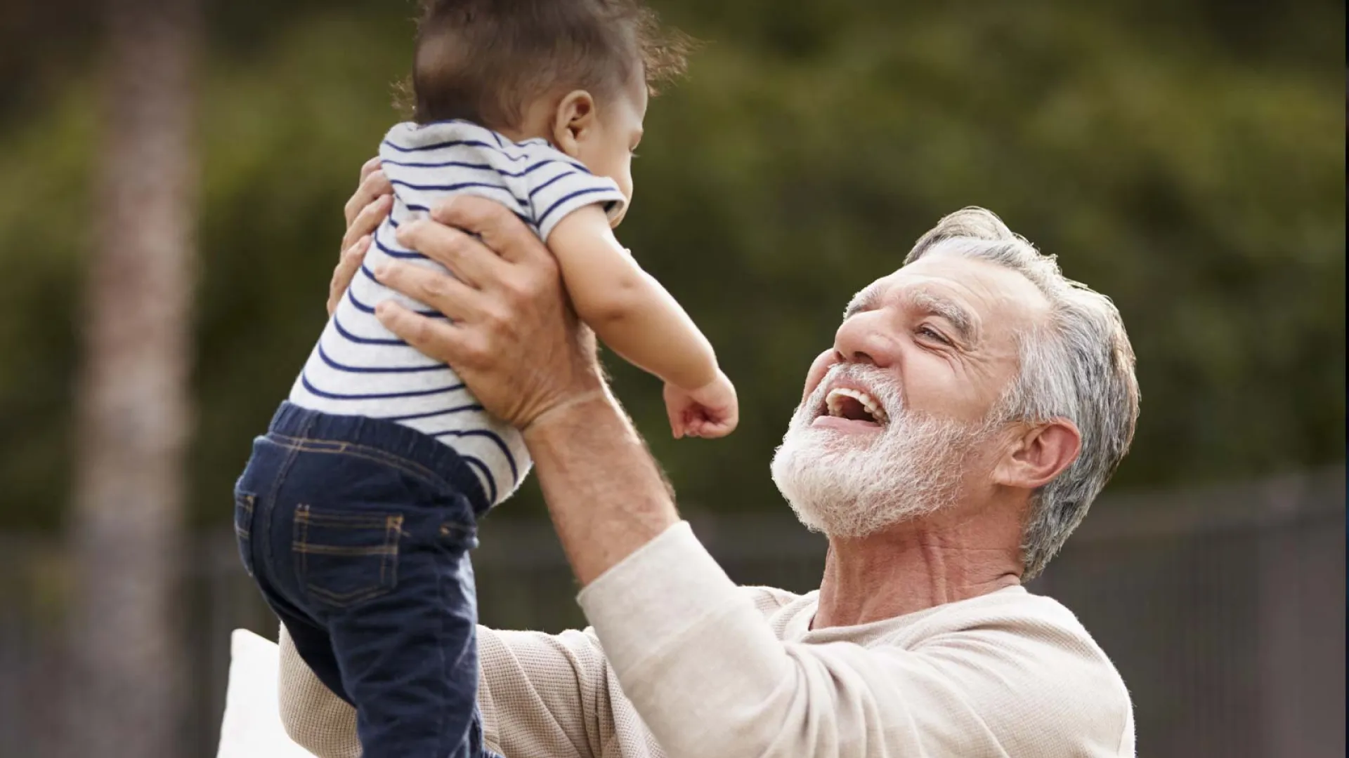 A joyful grandfather holding his smiling grandson outdoors, enjoying quality family time.