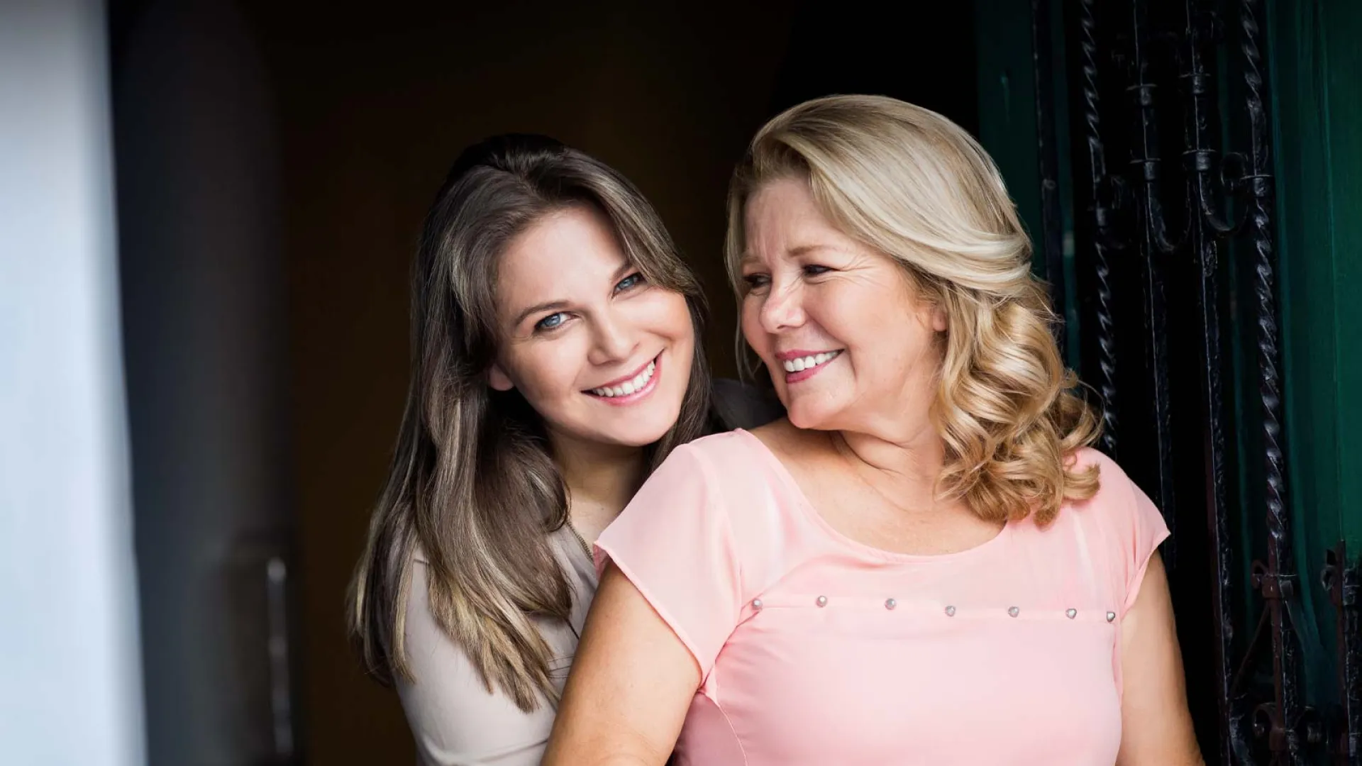 Two smiling women standing close together, showcasing warmth and affection in a well-lit setting.