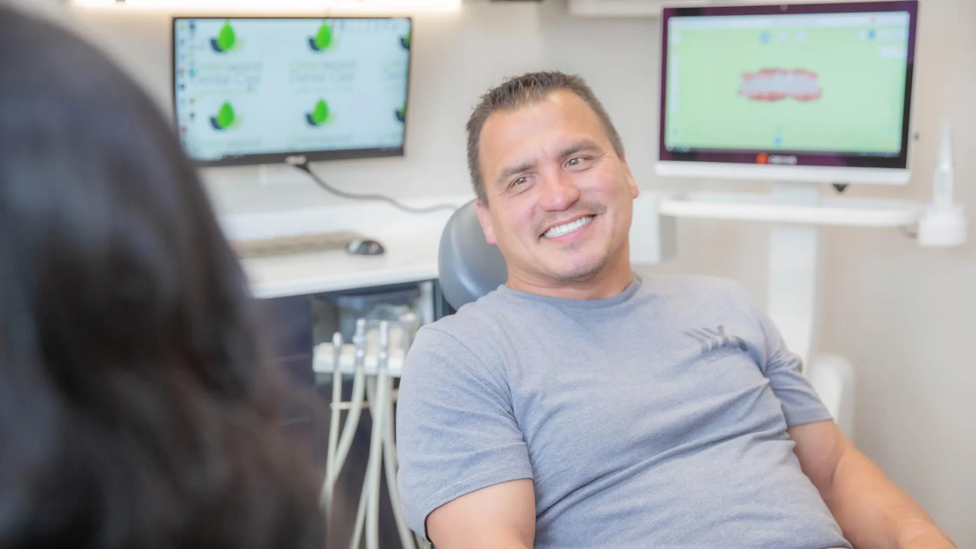 Smiling man sitting in a dental chair during a dental appointment with equipment and screens in the background