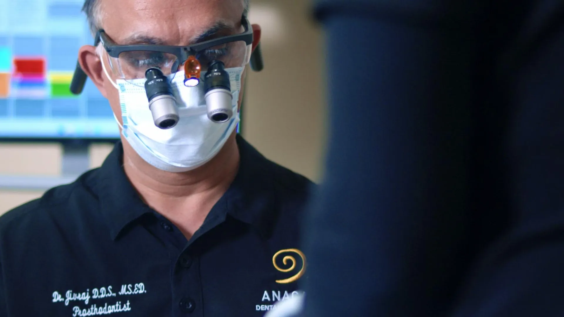Dentist wearing magnifying glasses and a mask while examining a patient in a modern dental office.