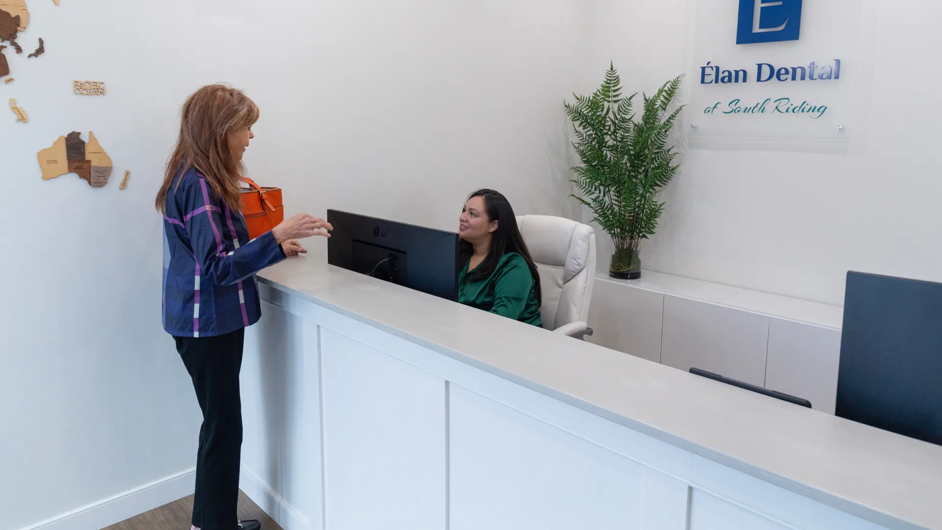 Woman talking to receptionist at Elan Dental South Riding with modern white reception desk and plant.