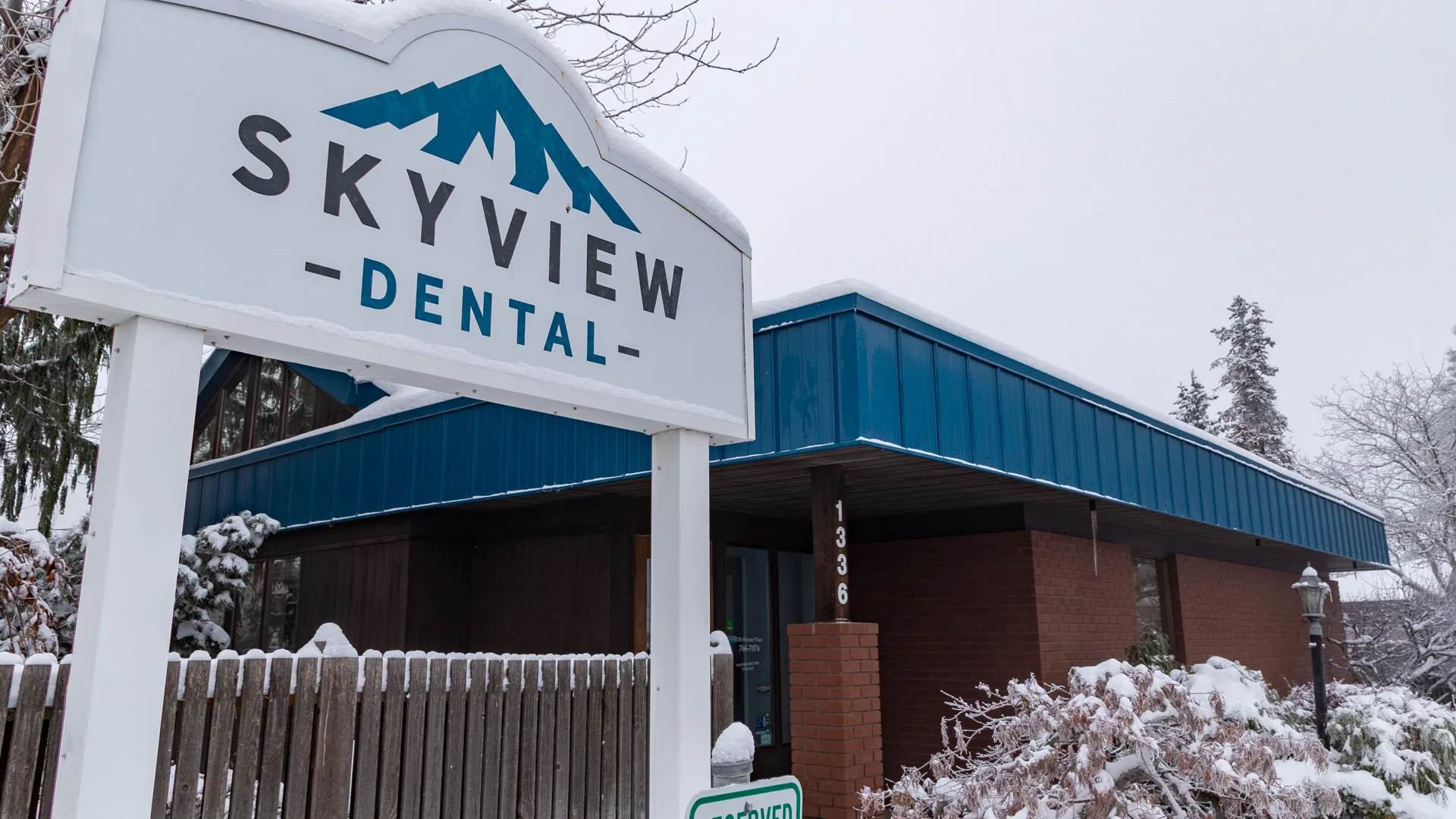 Skyview Dental sign and building covered with snow in a winter setting with trees and fence.