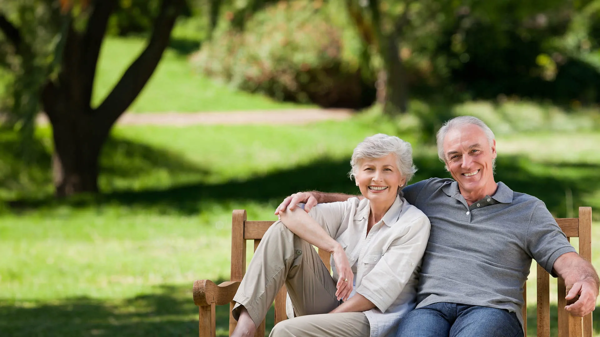an old man and woman sitting on a bench in a park