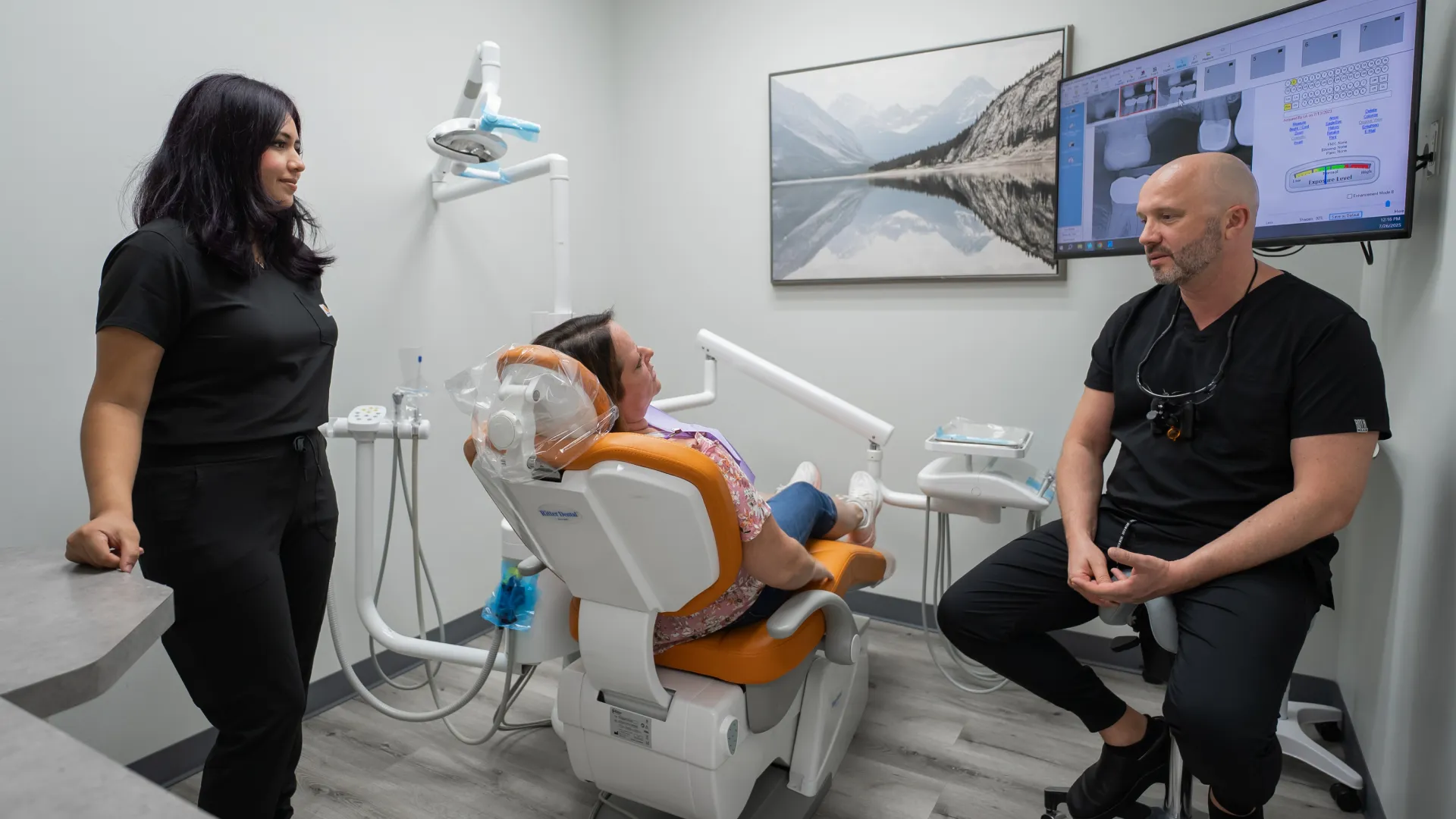 Dentist and assistant consulting a female patient in a modern dental clinic with digital X-ray displayed.
