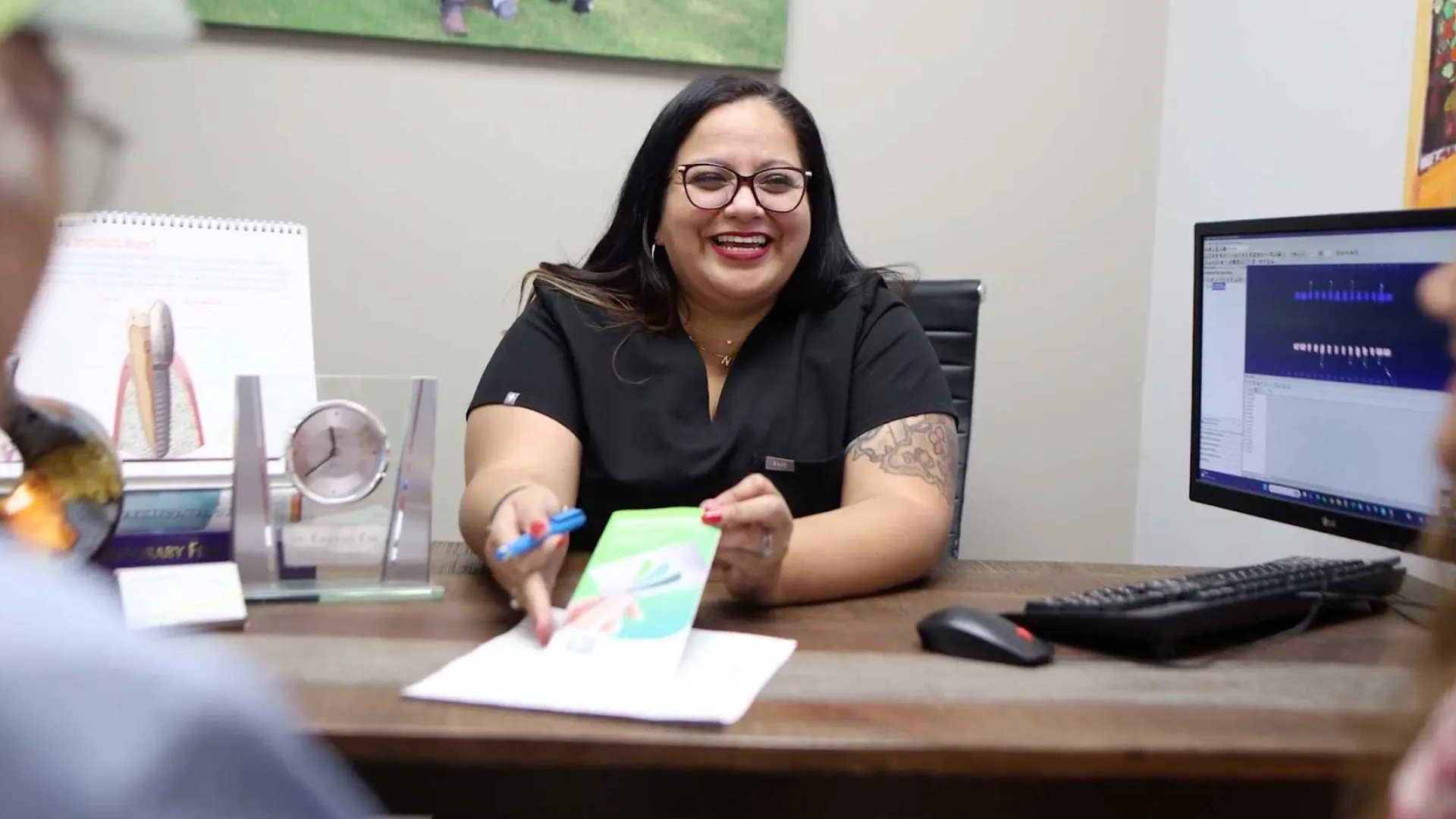 Smiling female medical professional explaining a health diagram to patients at an office desk with computer and documents