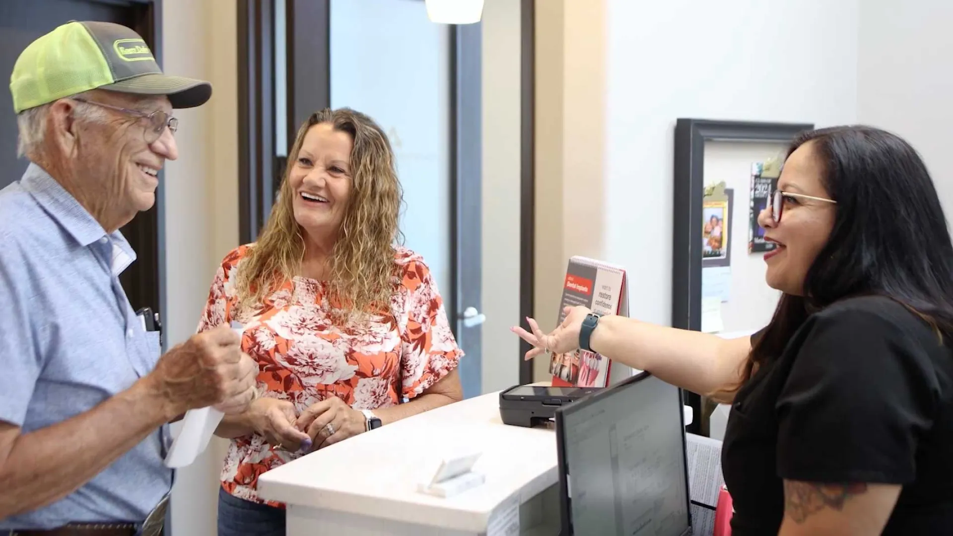 Smiling elderly man and woman talking with receptionist at a modern office reception desk