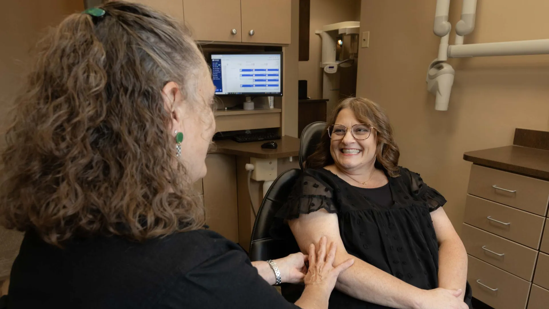 Woman smiling while sitting in a dental chair, consulting with a female dentist in a dental office.