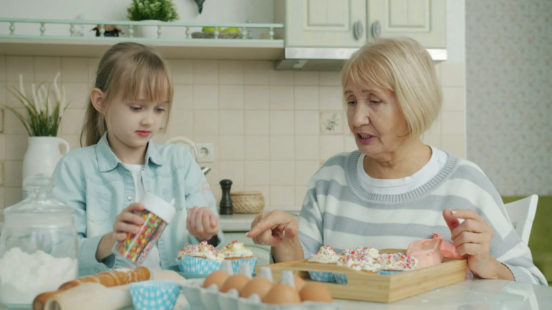 Grandmother and granddaughter decorating cupcakes together in a bright kitchen with baking ingredients on the table