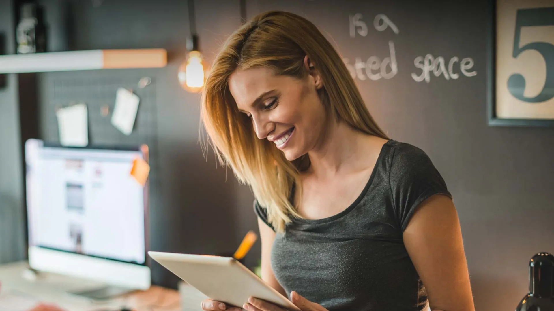 Smiling woman using a tablet in a modern office space with warm lighting.