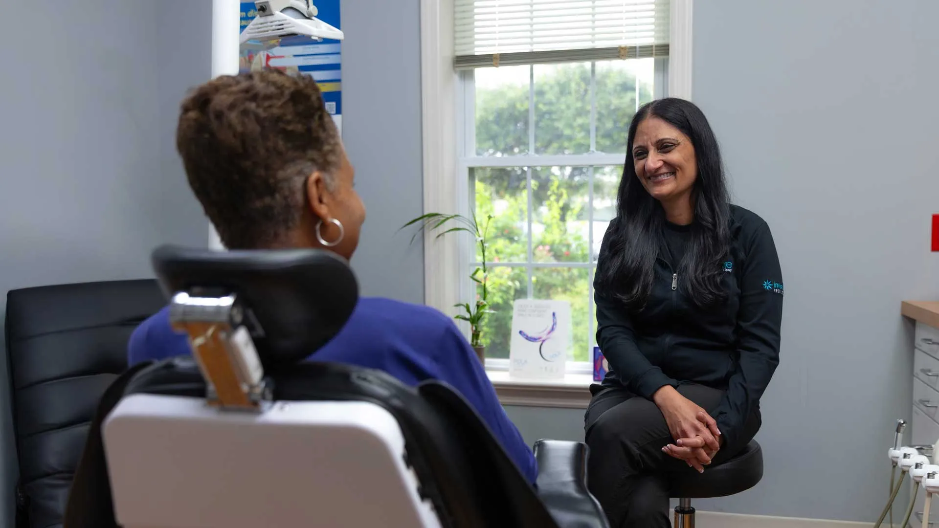 Dentist smiling and conversing with patient seated in dental chair in a bright clinic room