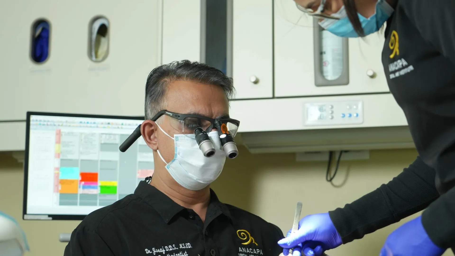 A dentist using magnifying glasses works on a patient's teeth in a modern clinic.