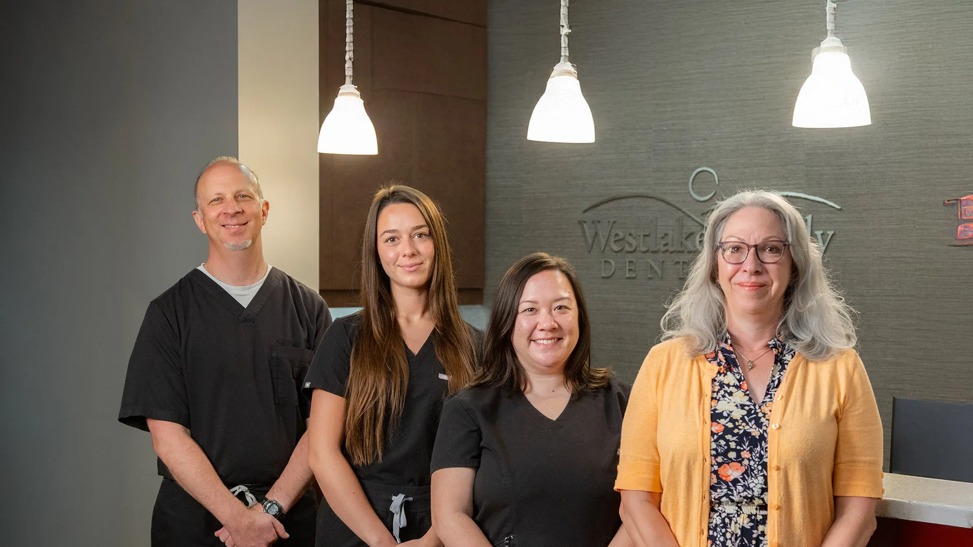 Four dental professionals smiling inside Westlake Family Dentistry office under hanging lights