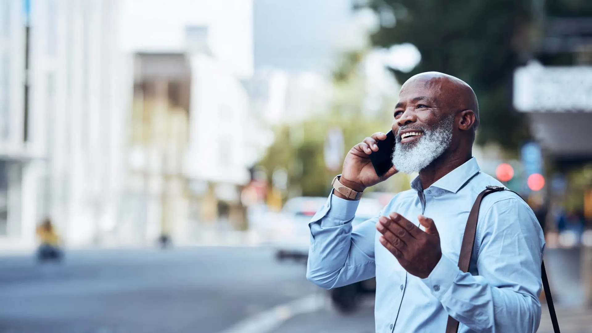 Smiling mature man with gray beard talking on smartphone outdoors in urban city environment.