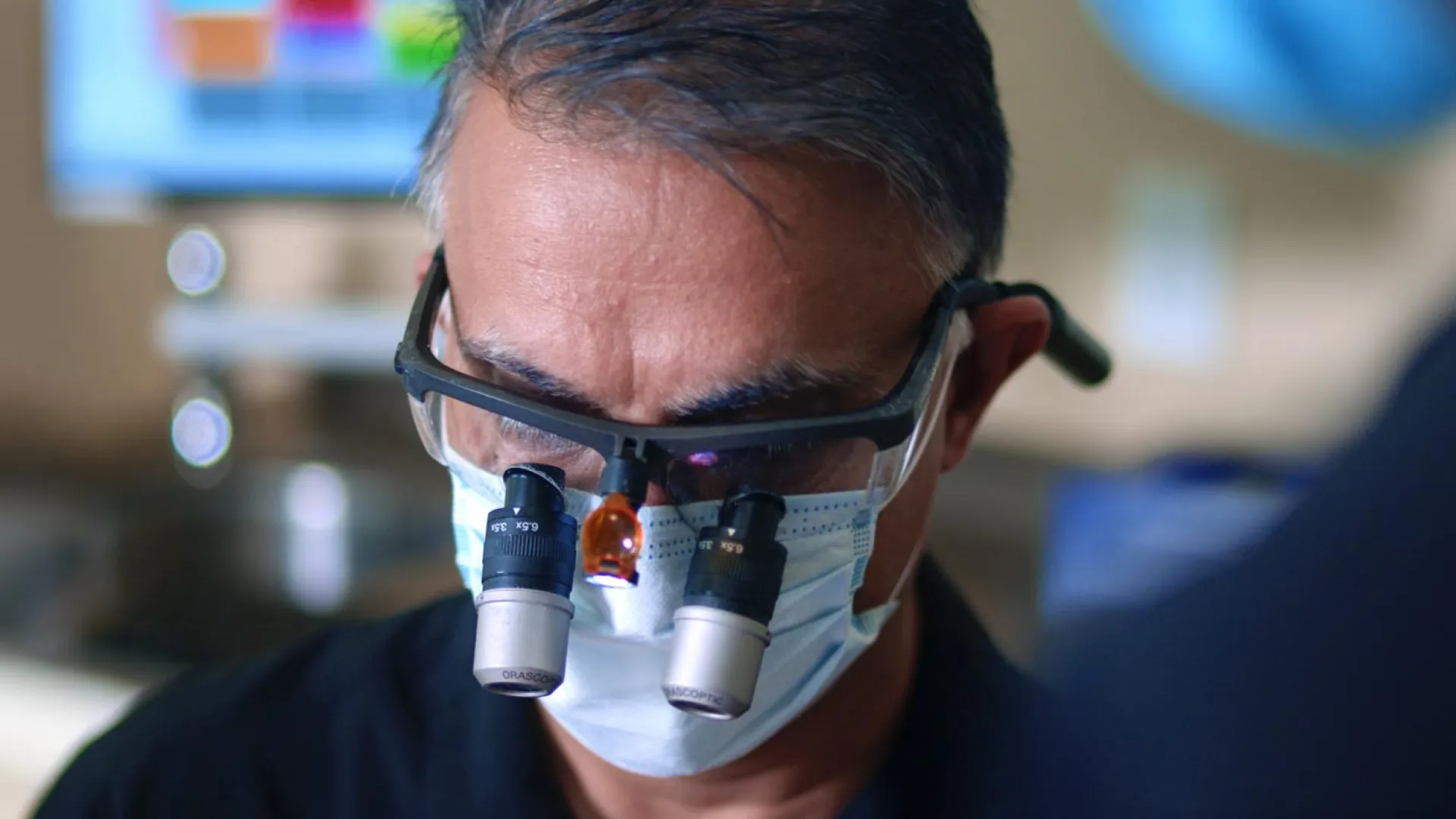 A dental professional wearing magnifying glasses and a mask during a procedure in a clinic.