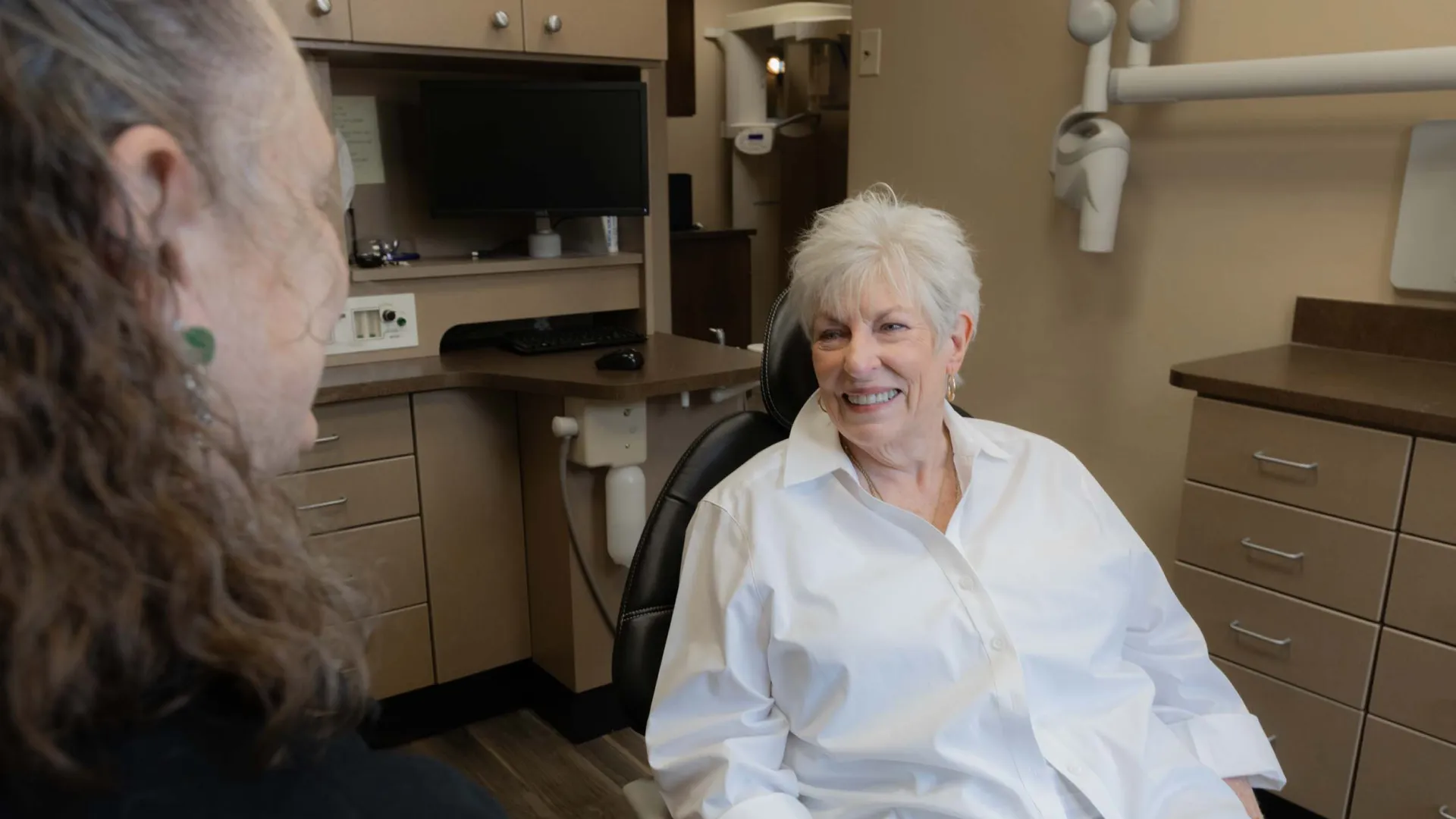 Senior woman smiling in dental chair during consultation with dentist in modern clinic room