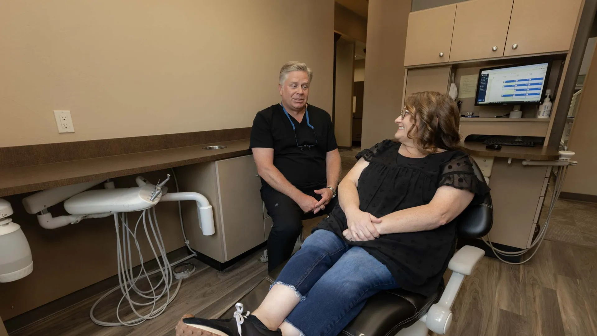 Dentist consulting with female patient seated in dental chair in a modern clinic room.