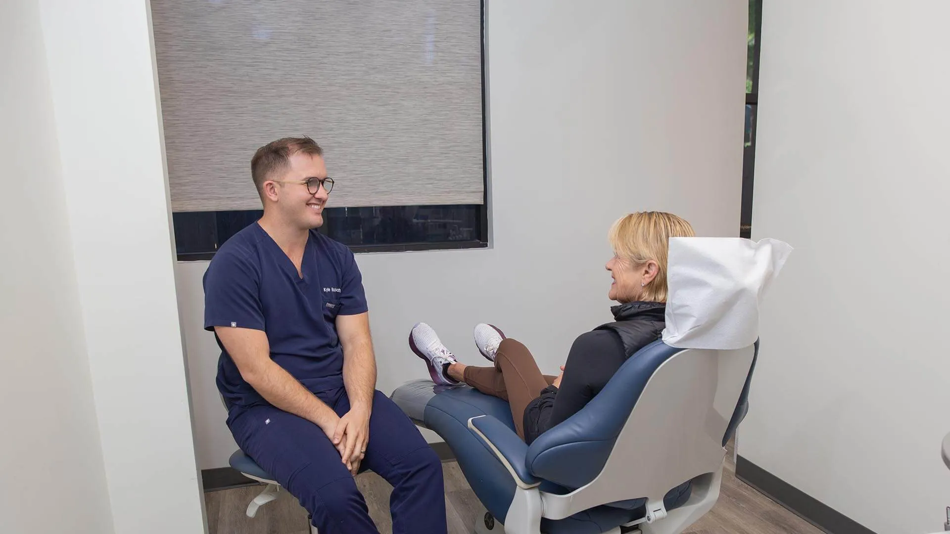 Dentist consulting a female patient in a modern dental office with a dental chair and neutral decor.