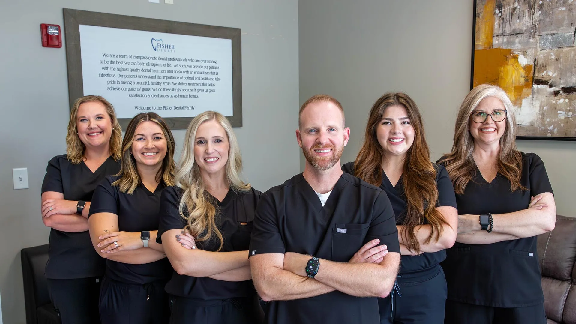 Smiling dental team in black scrubs standing with arms crossed in a modern office setting.