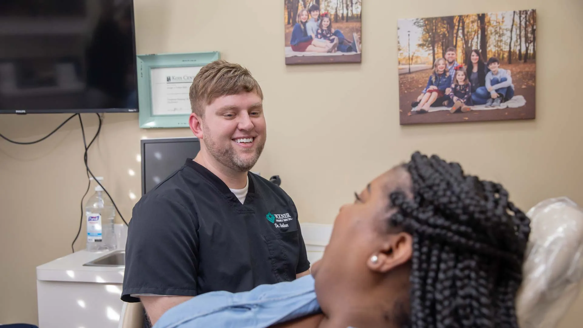 Male dentist smiling and talking to a female patient in a dental office with family photos on the wall