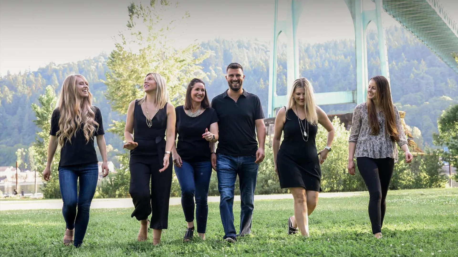 Group of six friends walking together in a park under a bridge on a sunny day.