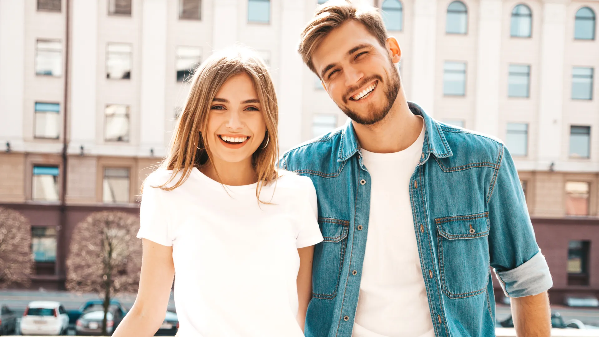 Young smiling couple dressed in casual denim and white shirts standing outdoors in urban setting