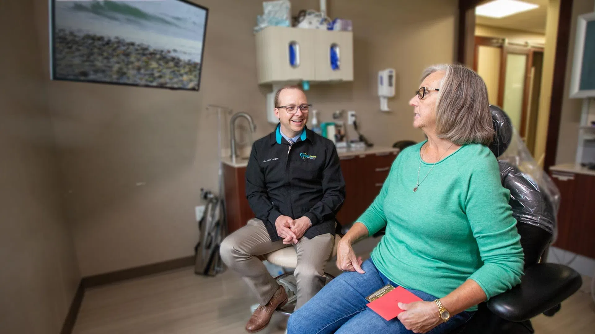A dentist converses with a patient in a well-lit dental office, showcasing a friendly atmosphere.
