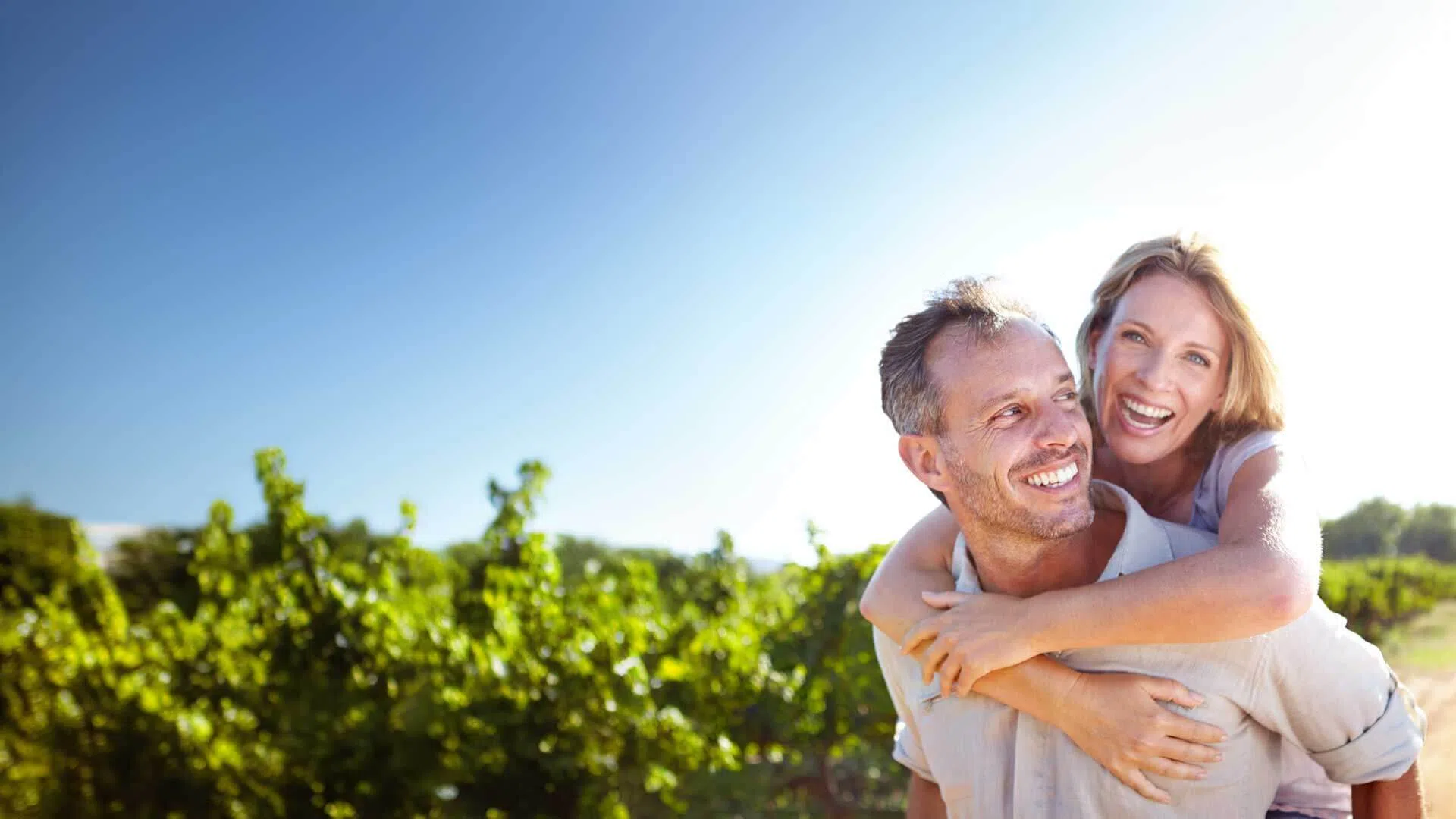Happy couple enjoying a sunny day outdoors with lush green vineyard in the background