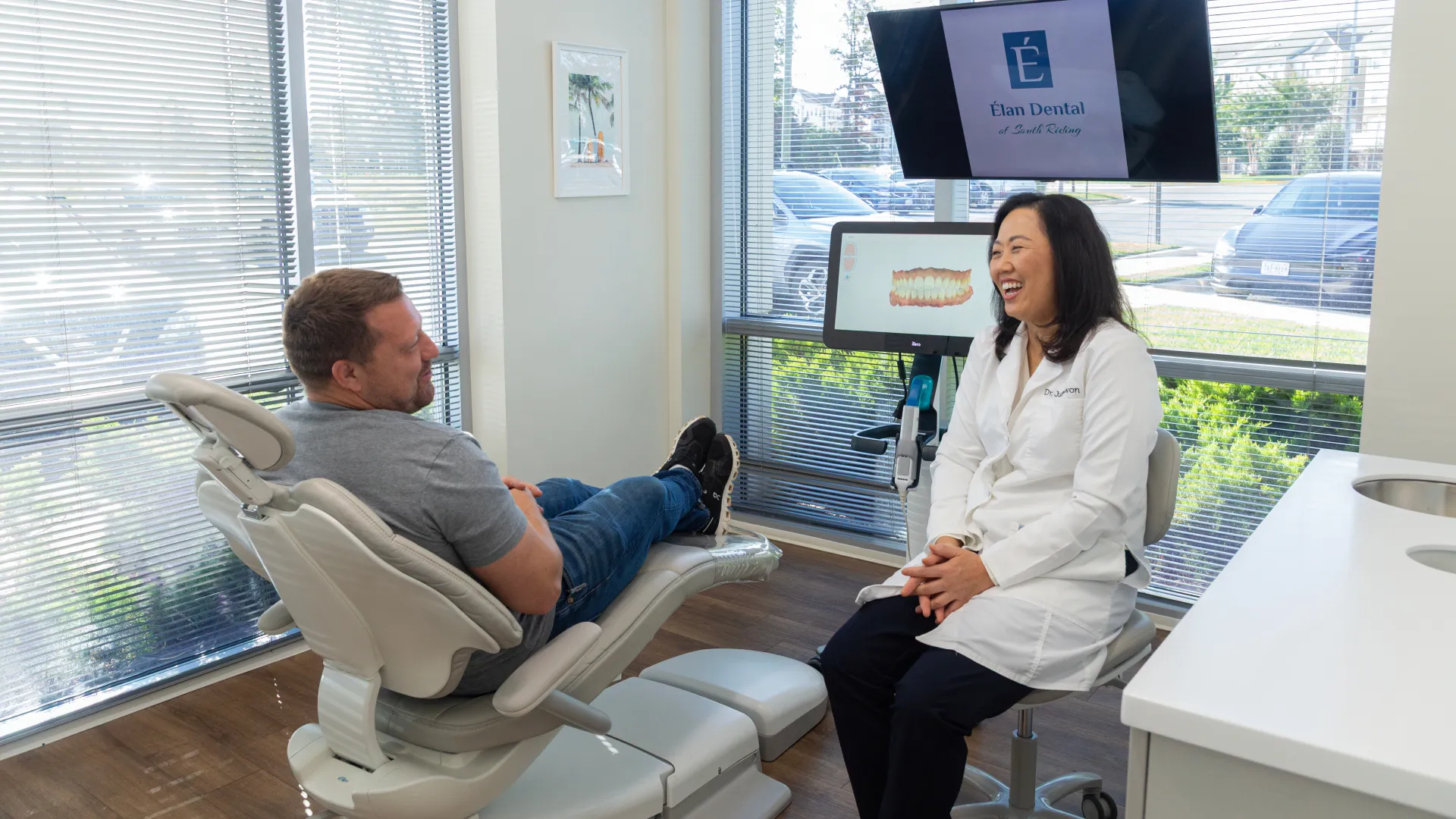 Dentist and patient smiling during a dental consultation in a modern clinic with digital imaging screens.