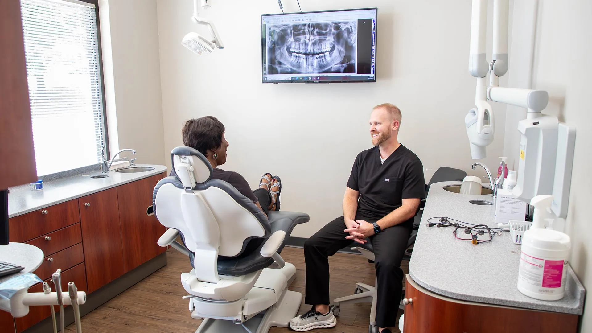 Dentist consulting with patient in modern dental office with dental chair and tooth X-ray on screen