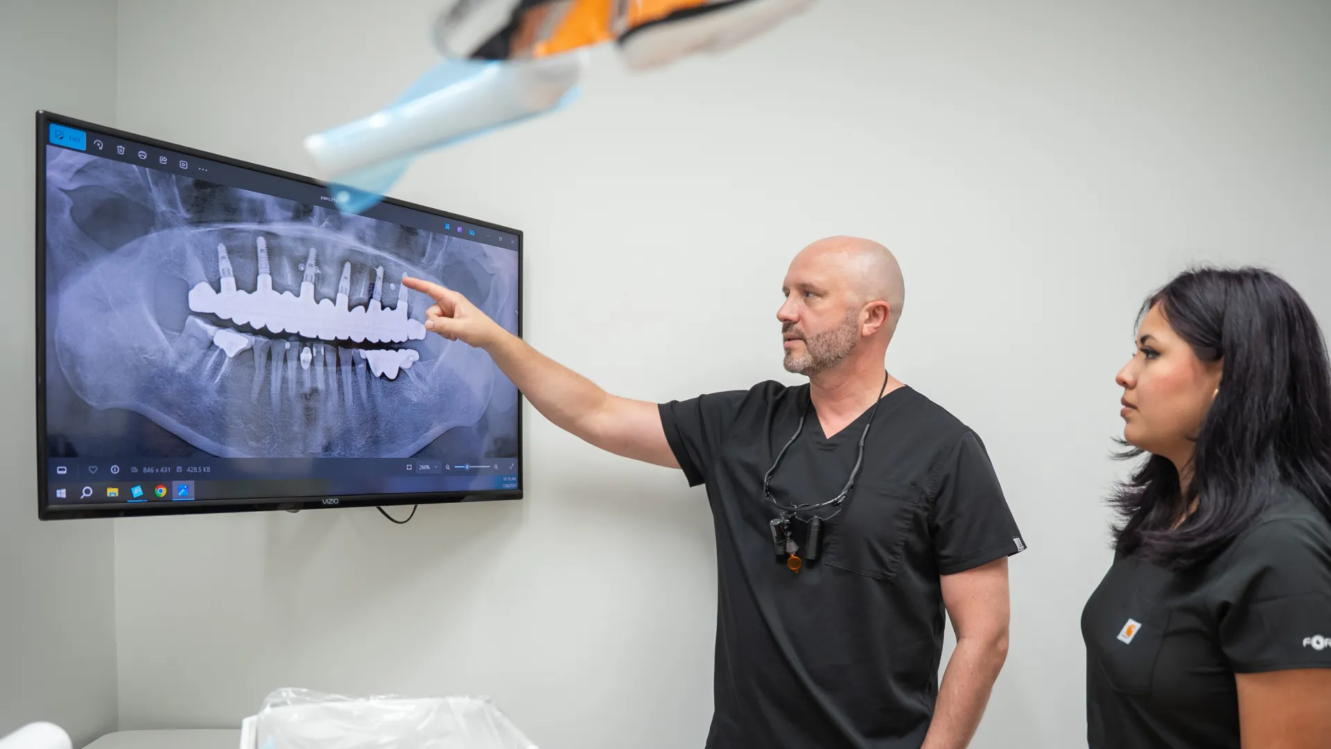 Dentist explaining dental X-ray with implants and crowns to patient in consultation room.