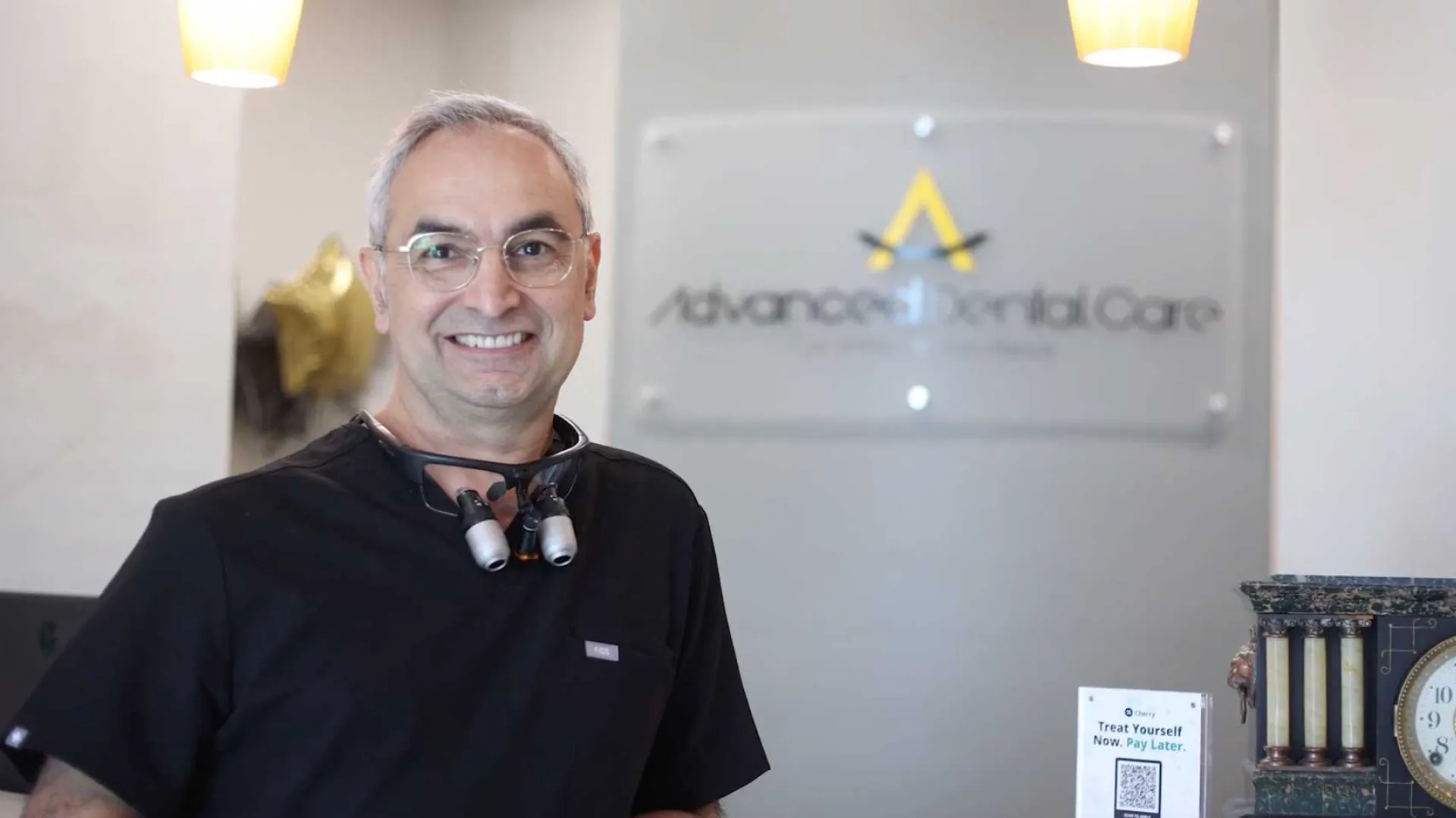Smiling male dentist with dental loupes around neck in modern dental office reception area