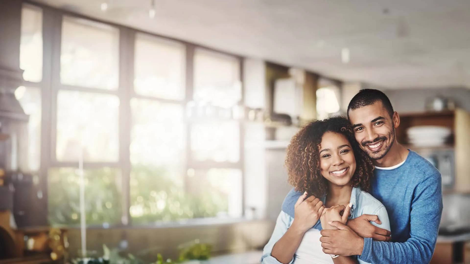 Happy couple embracing in a bright kitchen setting, showcasing love and joy at home.