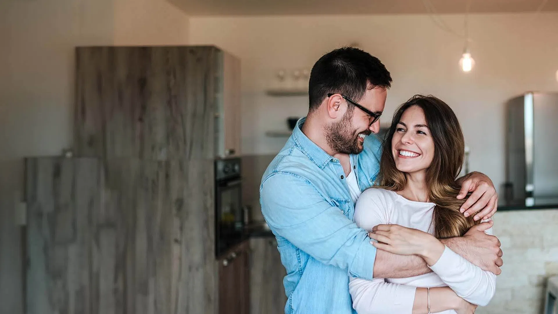 Happy couple embracing and smiling in a modern kitchen with cozy warm lighting