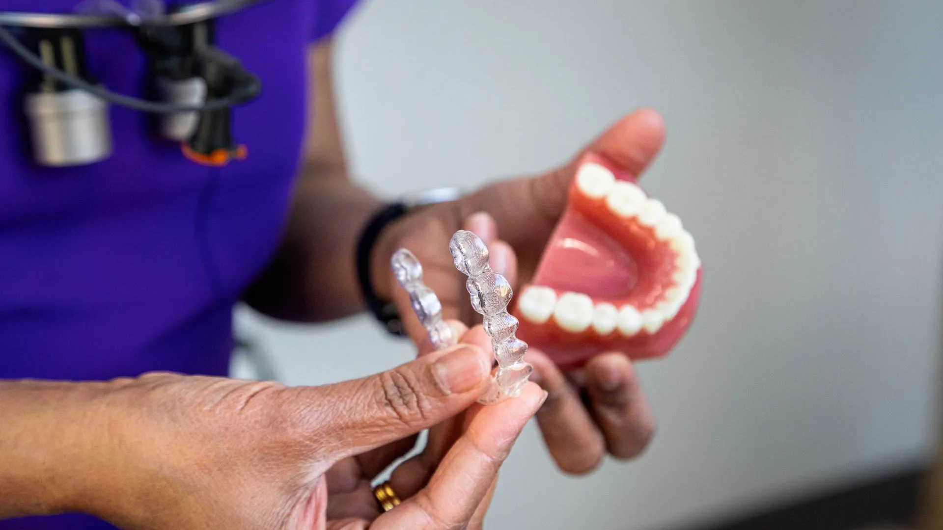 Dentist holding clear aligners and a dental model showing teeth and gums for orthodontic treatment.