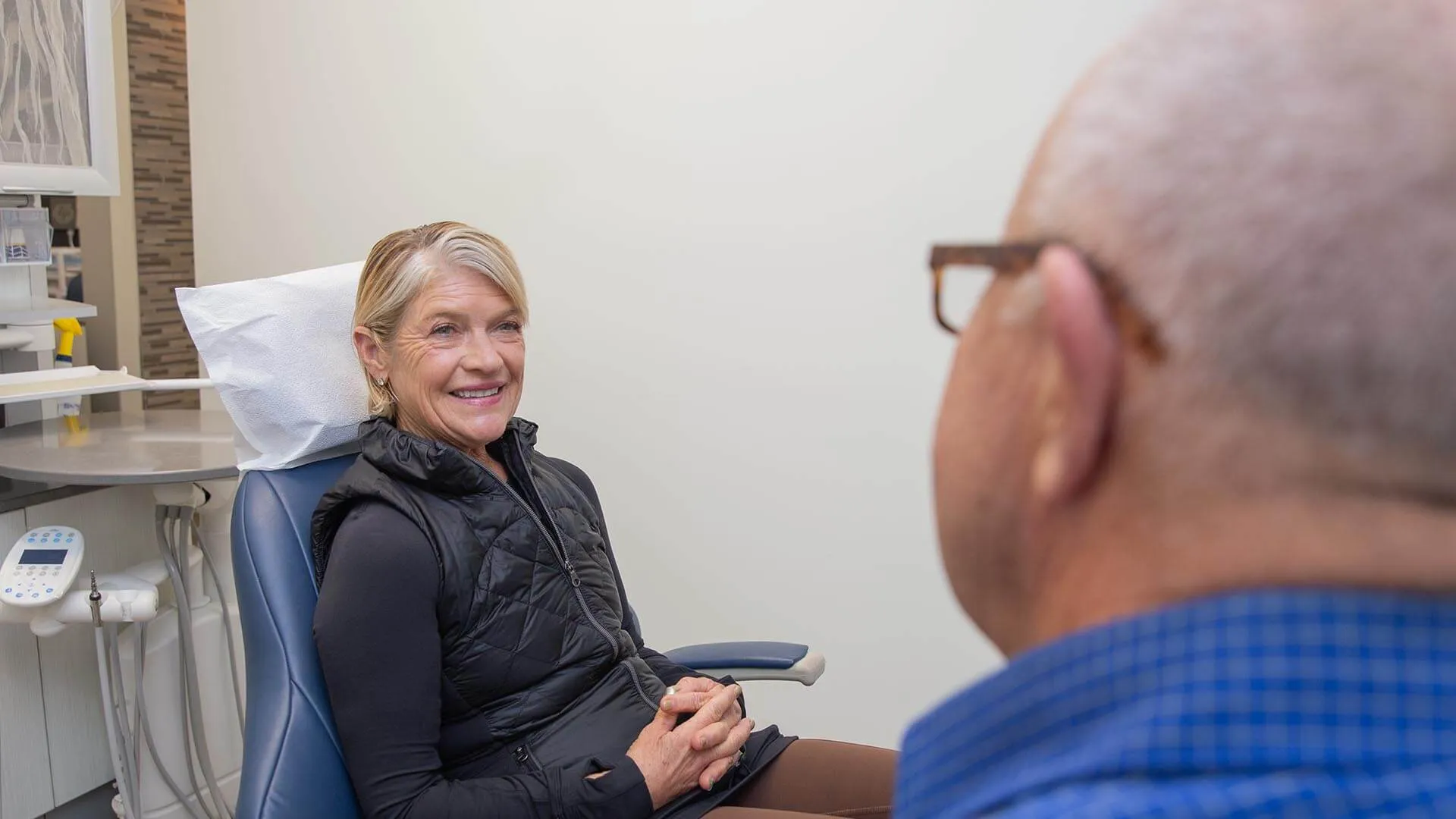 Smiling woman sitting in dental chair talking to male dentist in clinic with medical equipment nearby