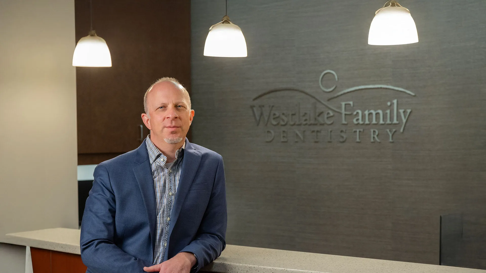 Man in blue blazer standing in front of Westlake Family Dentistry reception desk with lit hanging lamps