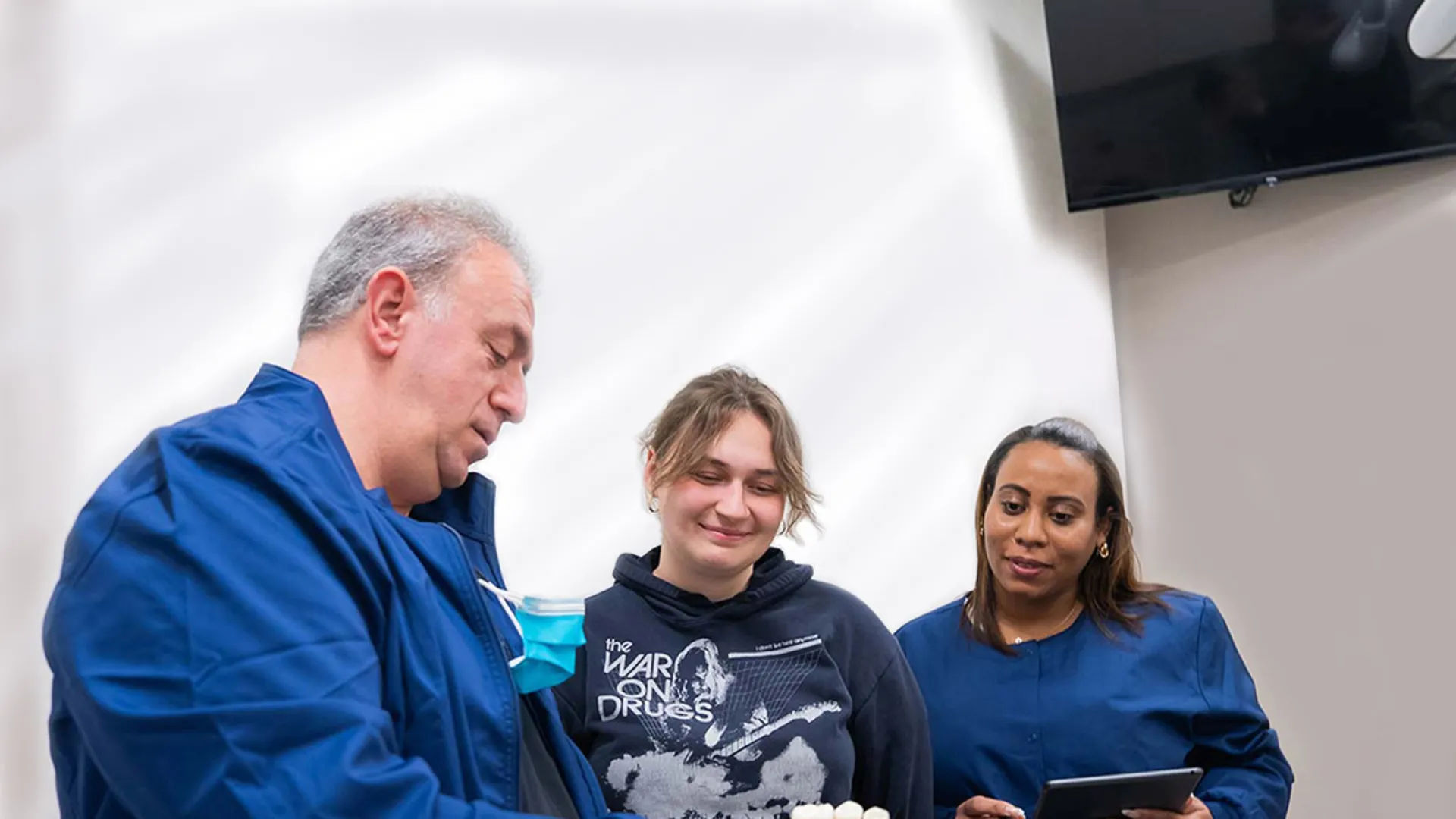 Medical professionals in blue scrubs reviewing a patient's records with a young woman in casual clothing indoors.