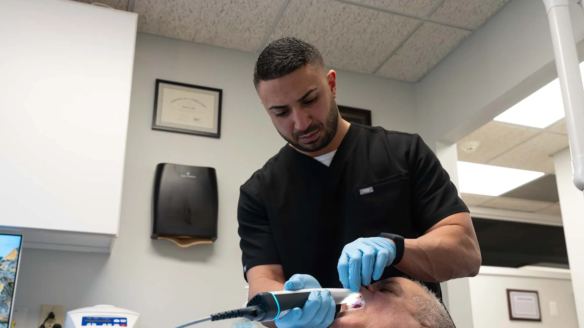 Dentist in black scrubs examining patient's teeth using dental device in modern clinic.
