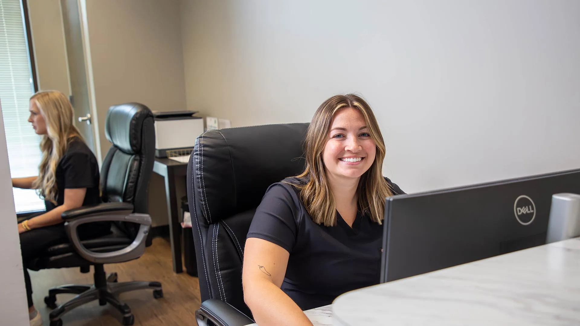 Smiling woman sitting at her desk working on a Dell computer in a modern office environment.