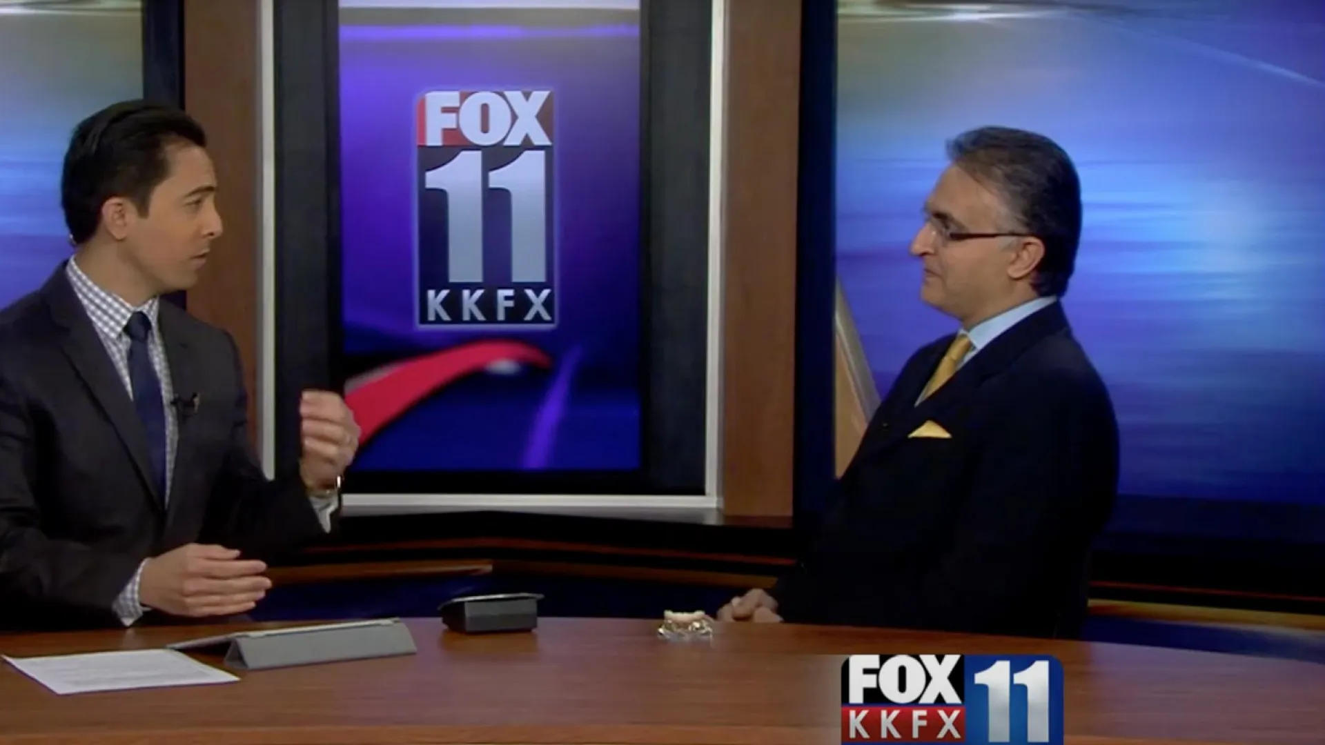 two men discussing on a studio set with FOX 11 logo backdrop.