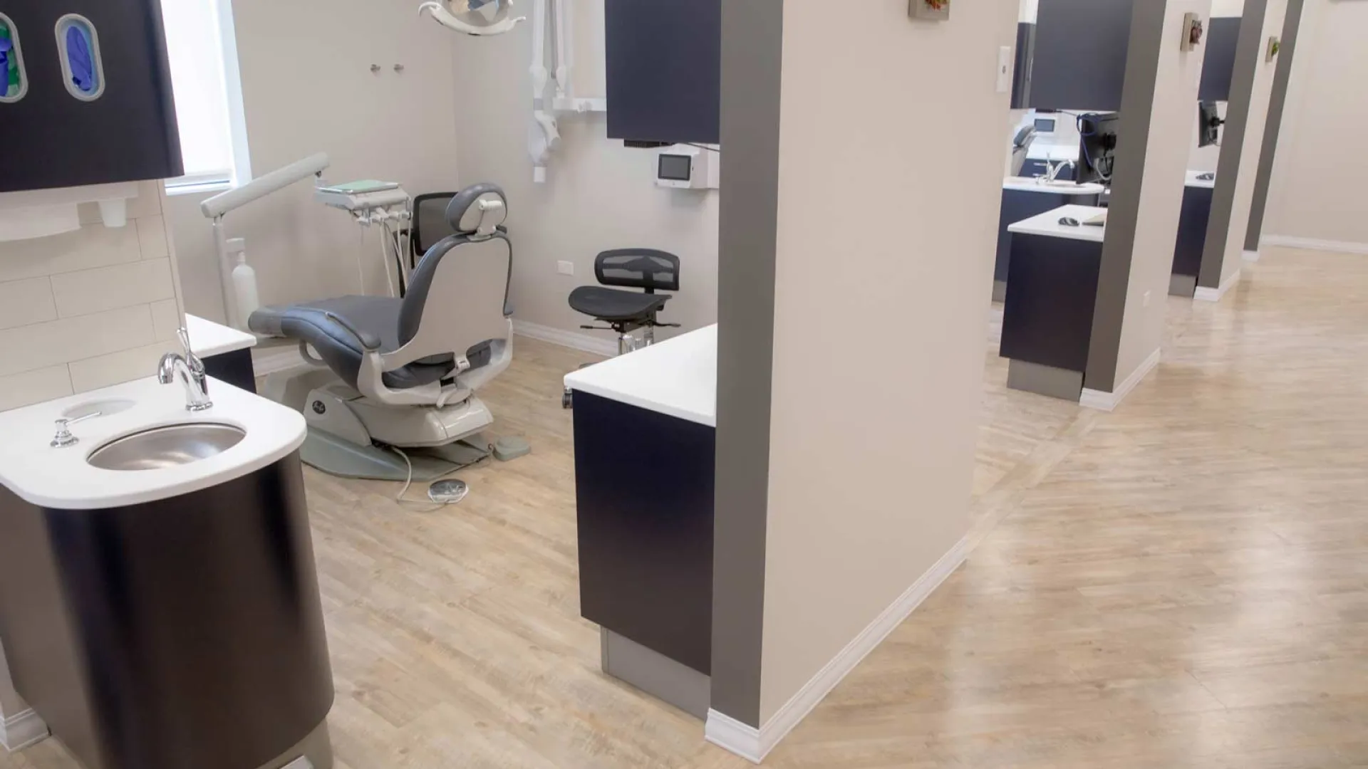 Modern dental office with treatment chairs, sinks, and clean, bright interiors and wooden flooring.